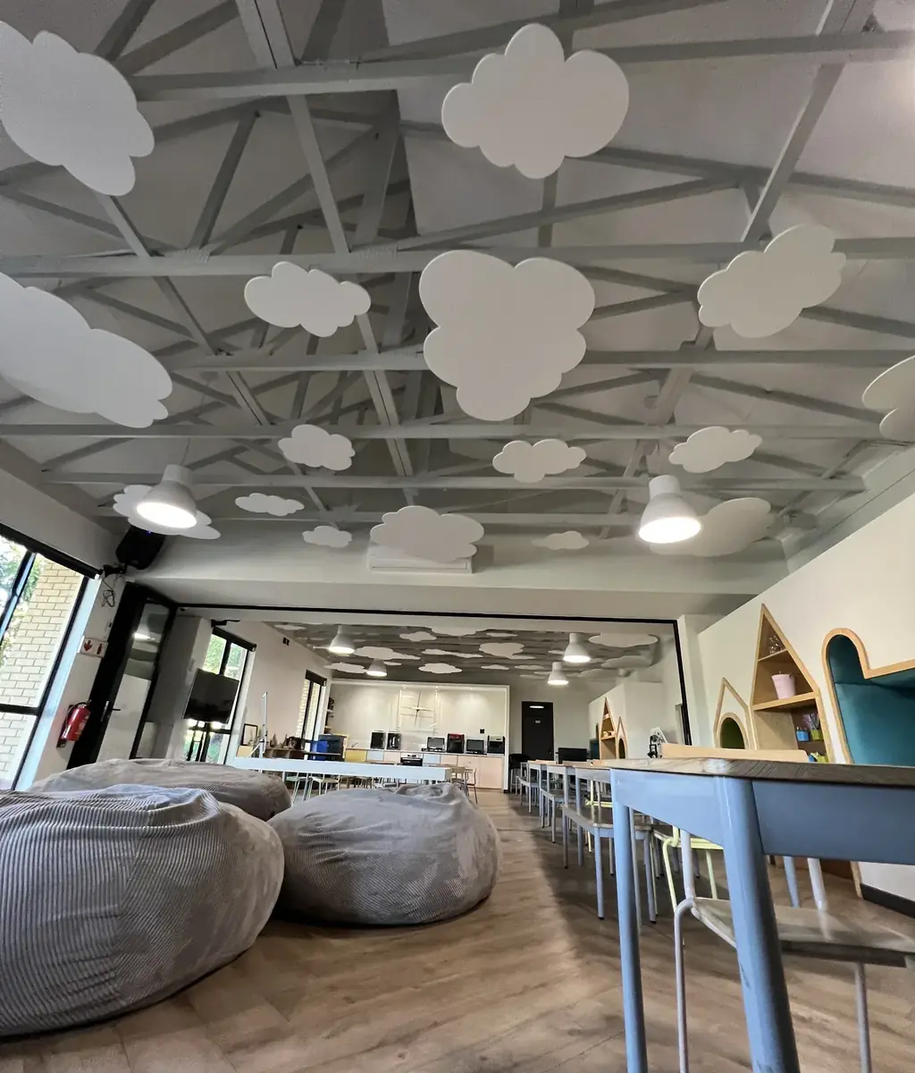 White felt clouds below the roof trusses of a bright school learning space, with beanbags and tables underneath