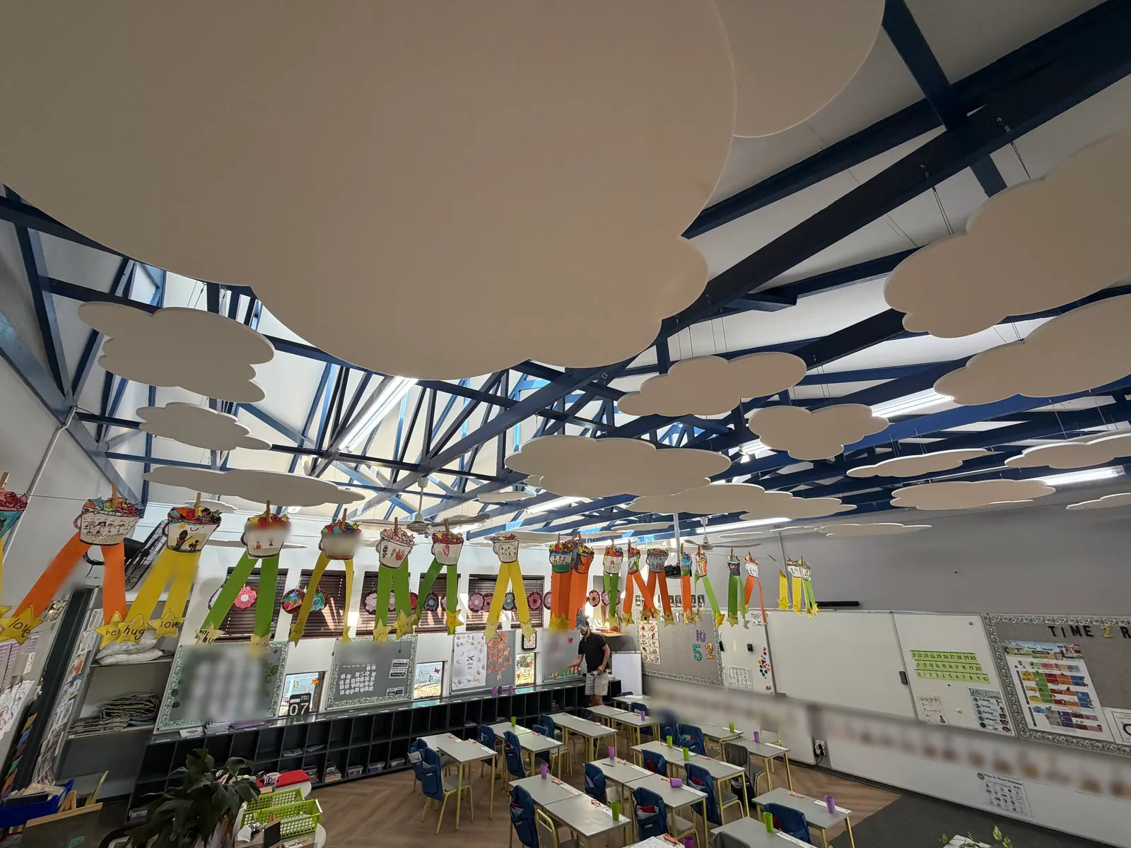 White felt clouds above a classroom, with children's paper artwork hanging on a line below them