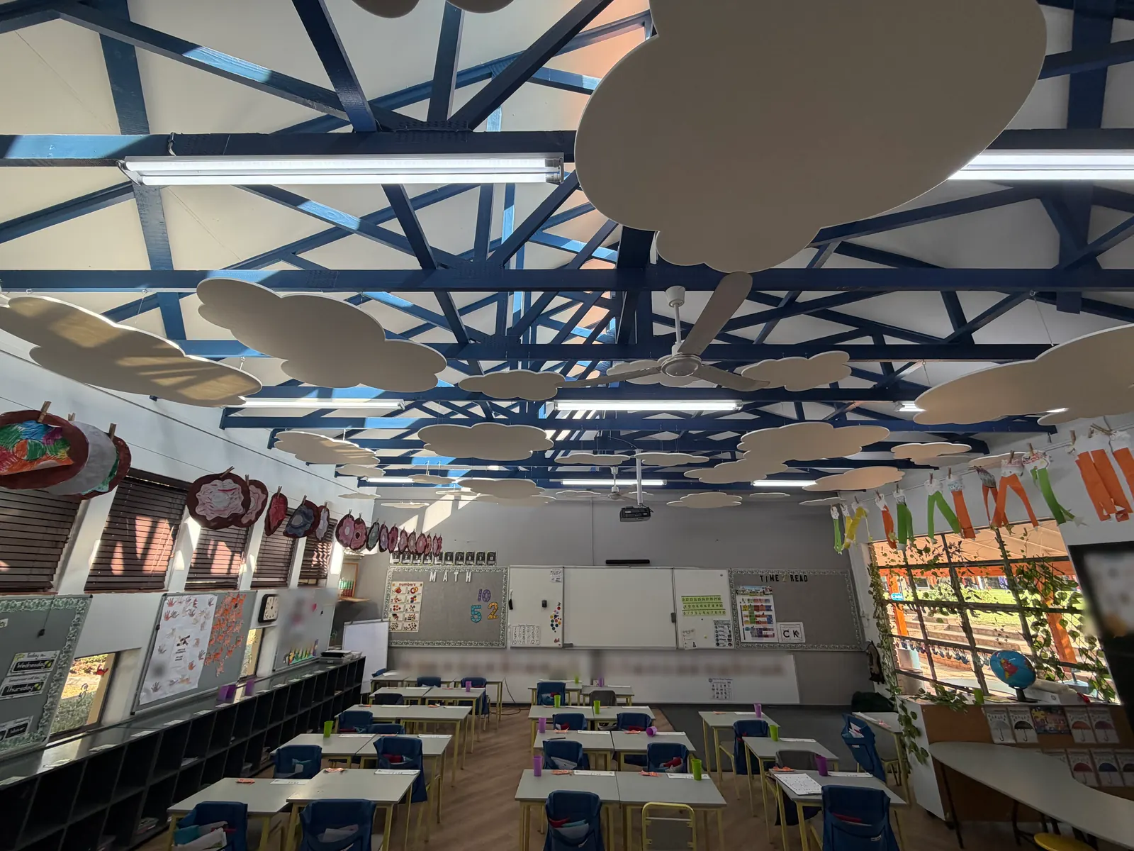 A classroom with rows of desks under white felt clouds hung between blue roof trusses