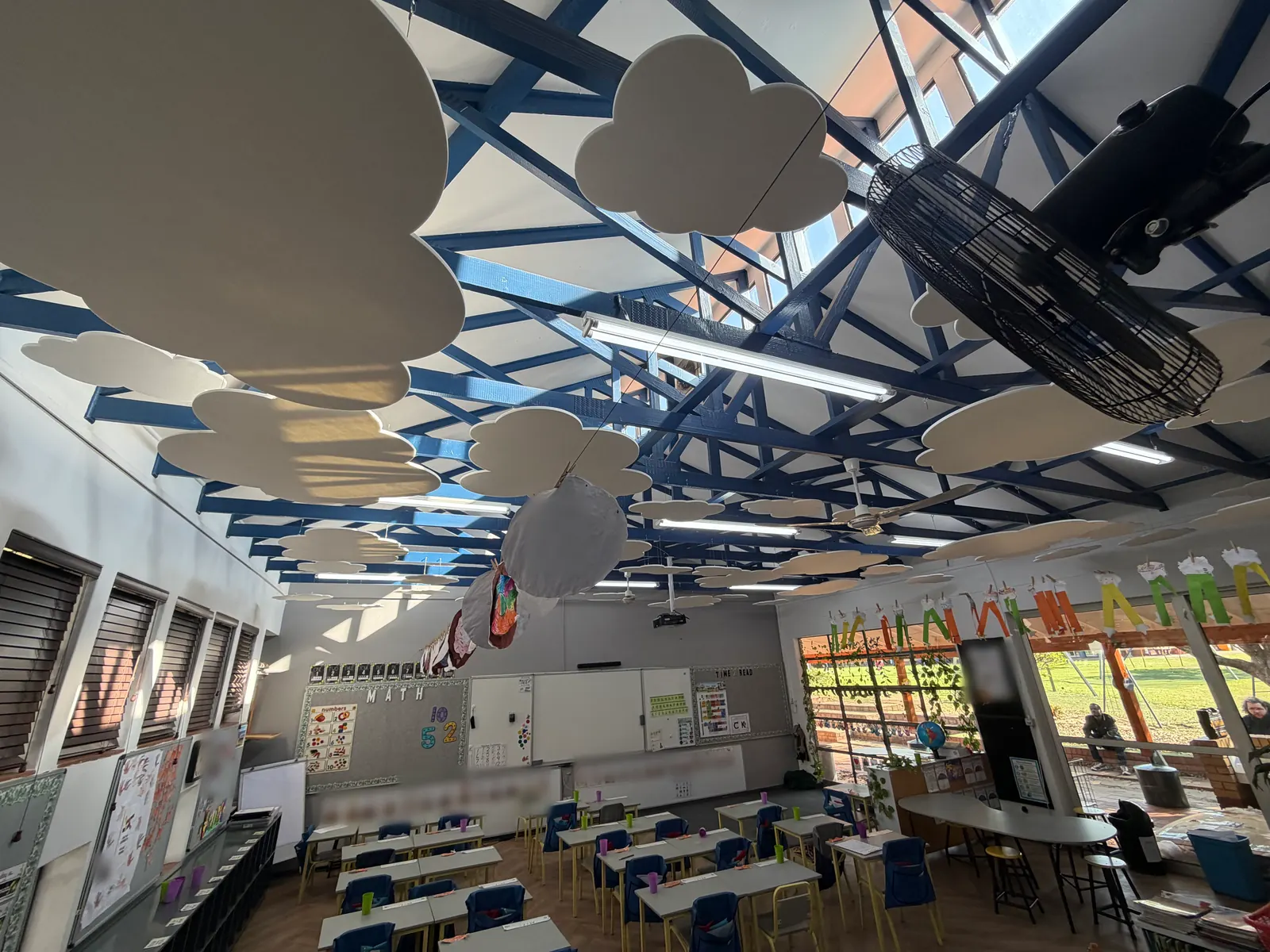 Afternoon sun across a classroom ceiling hung with white felt clouds, a fan and a projector