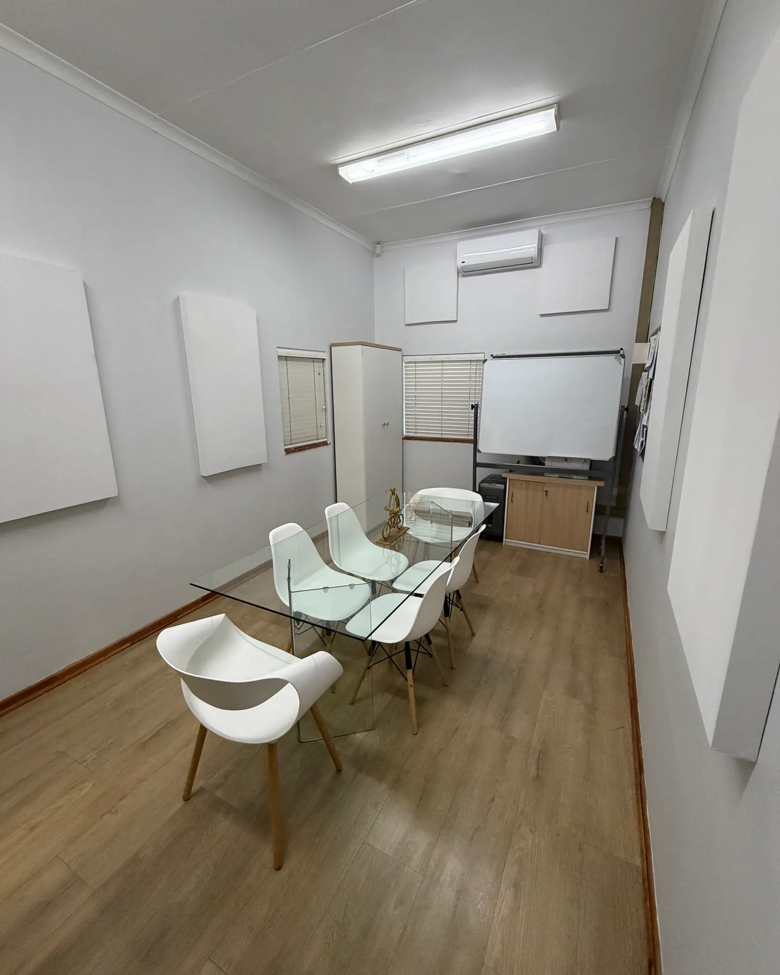 A narrow meeting room with large white panels on both long walls and two square panels above the whiteboard