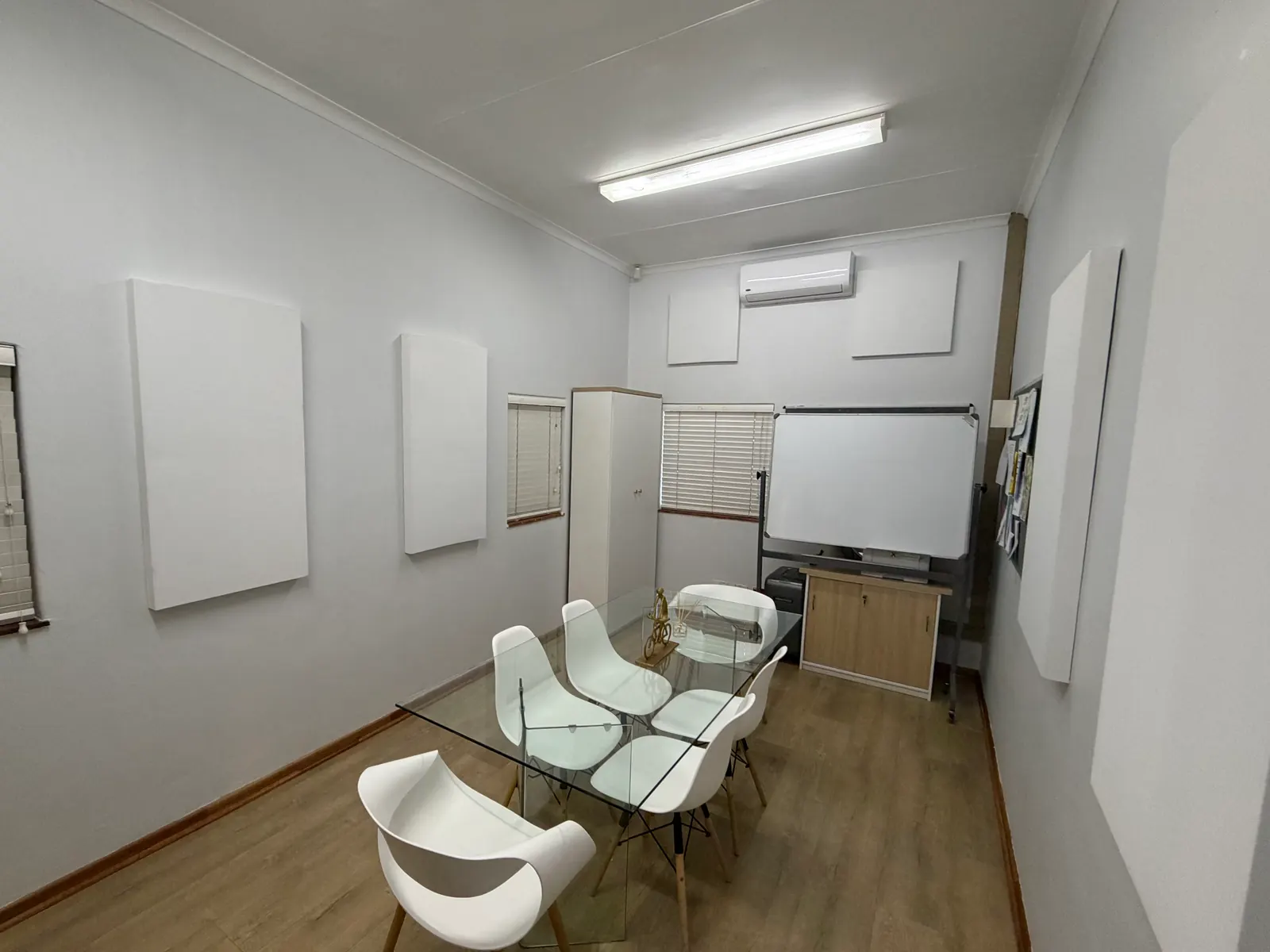 A small meeting room with a glass table and white chairs, and white acoustic panels on the walls